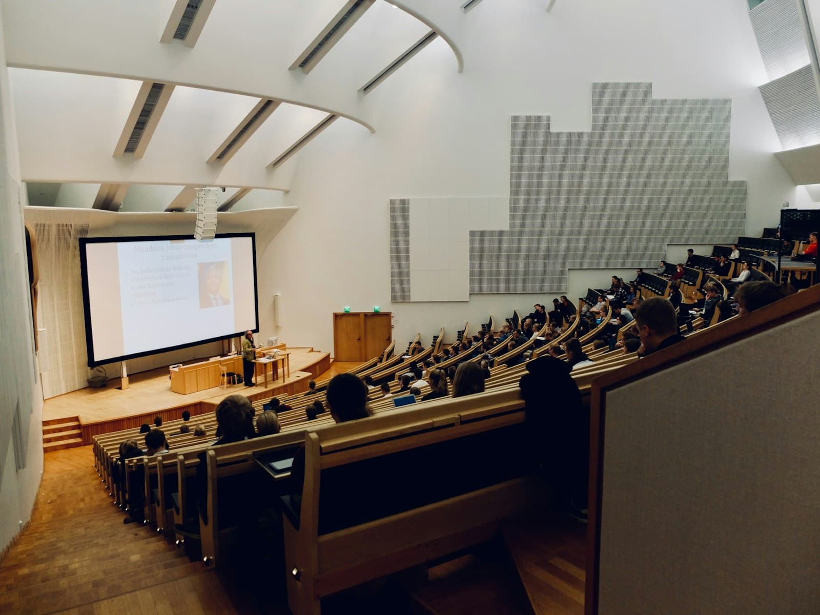 Rows of students at desks face the front of a tiered university lecture hall
