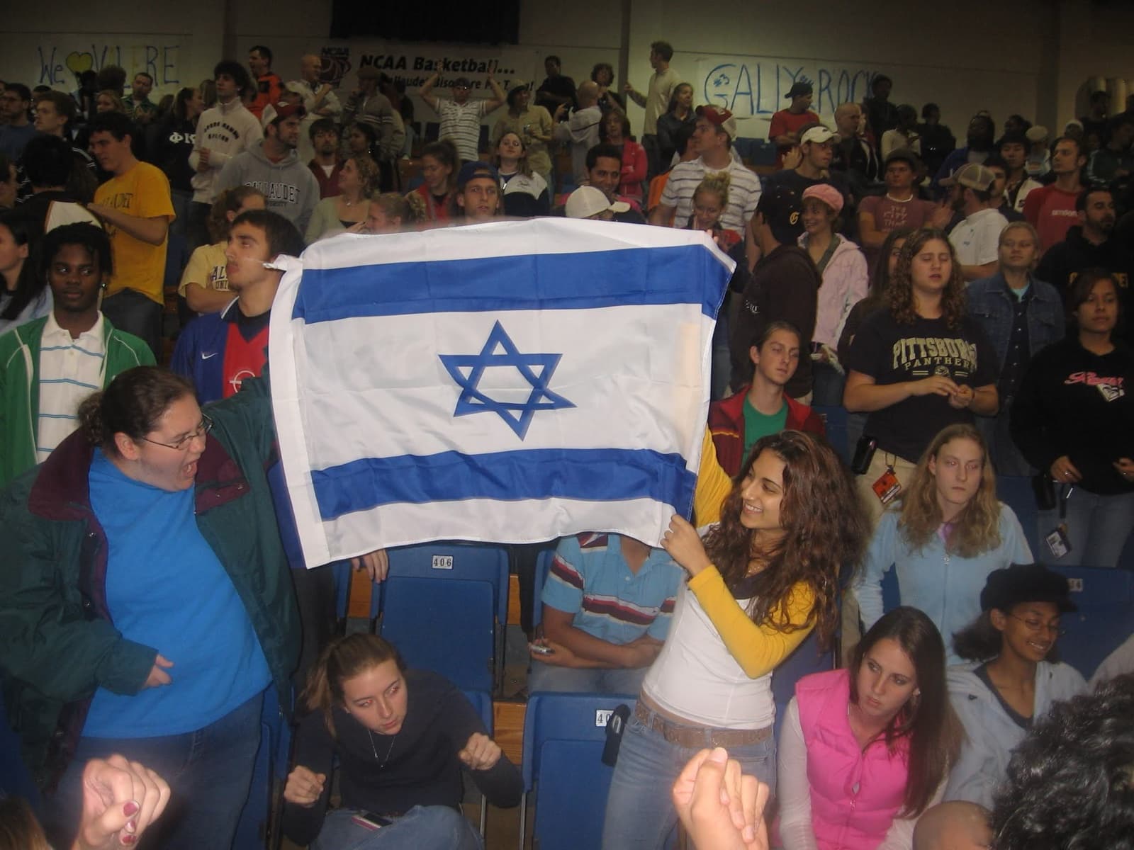 American college students in the stands holding up an Israeli flag during a game.