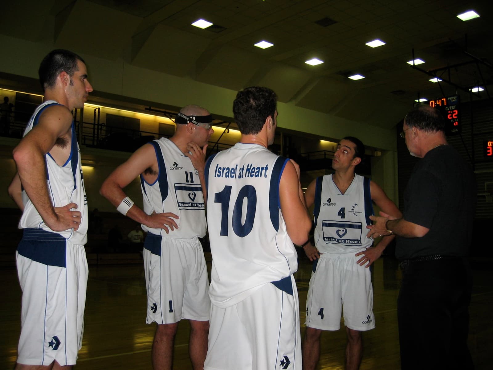 Israeli players in a courtside huddle with their coach, Israel at Heart across their jerseys.