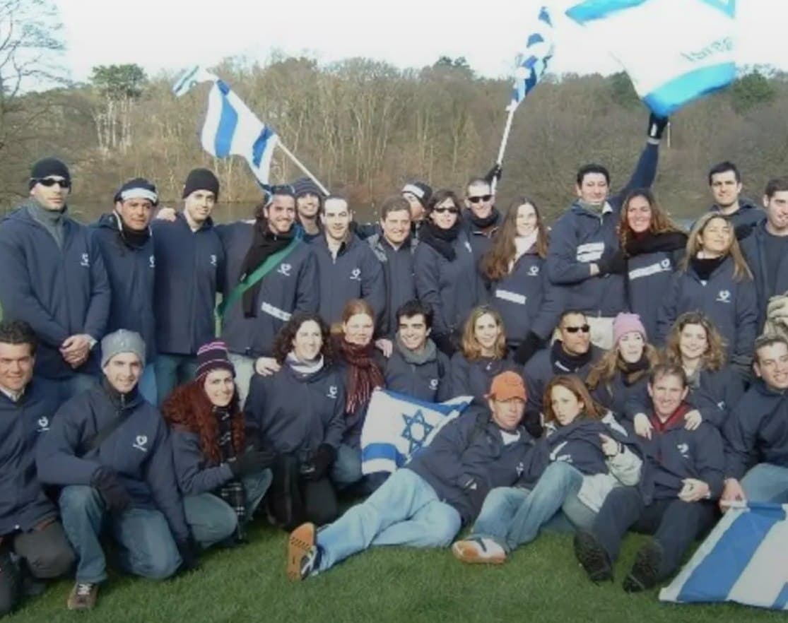 Israel at Heart delegates in matching jackets waving Israeli flags outdoors in winter.