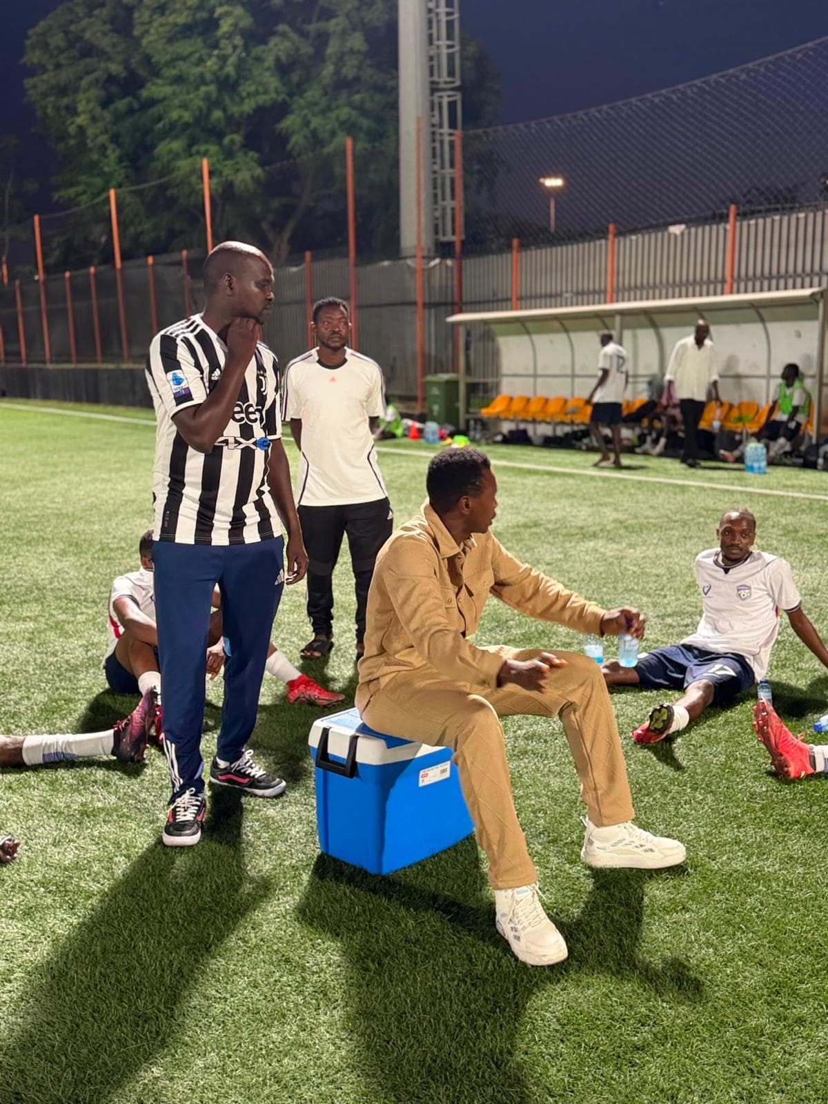 Players resting together on the pitch under floodlights after a game.