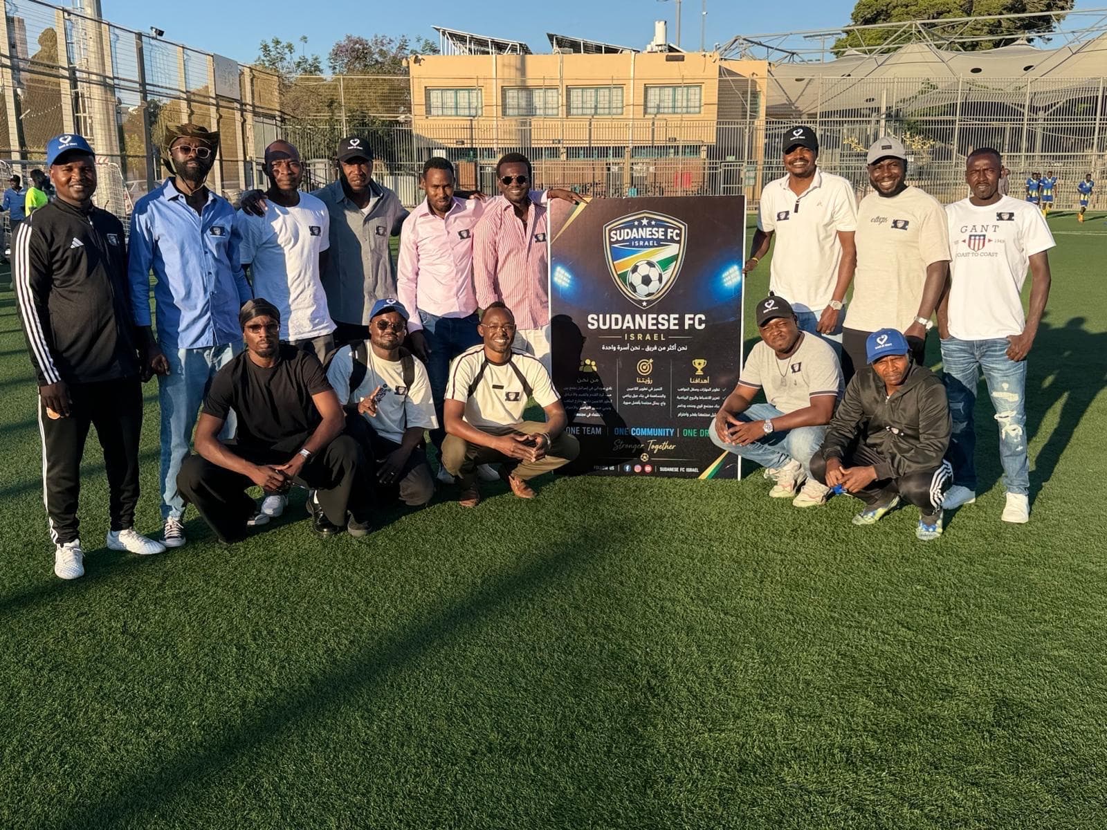 Members of Sudanese FC Israel gathered around their club banner, which reads one team, one community.