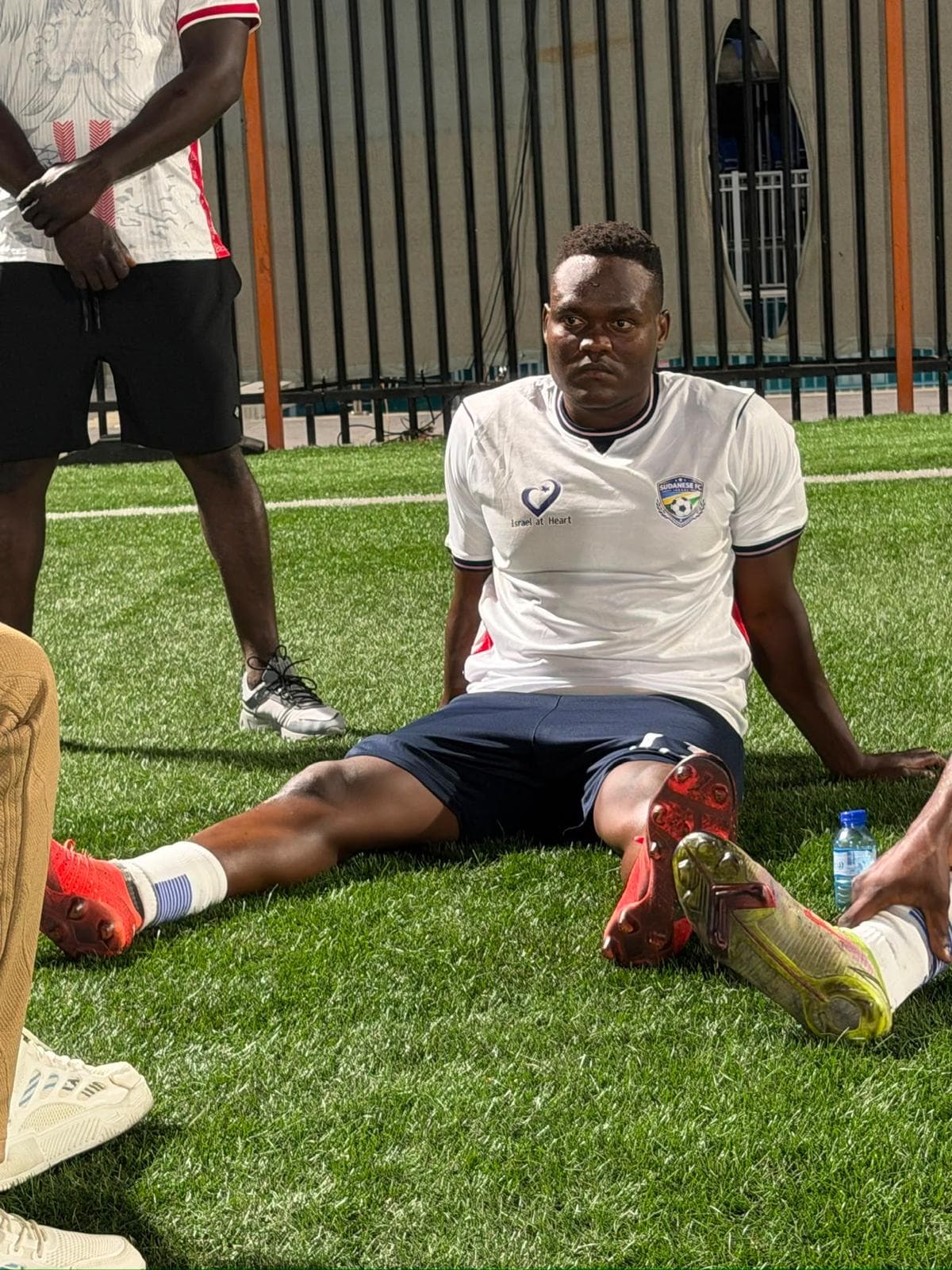 A player in a white kit bearing both the Israel at Heart and Sudanese FC crests.