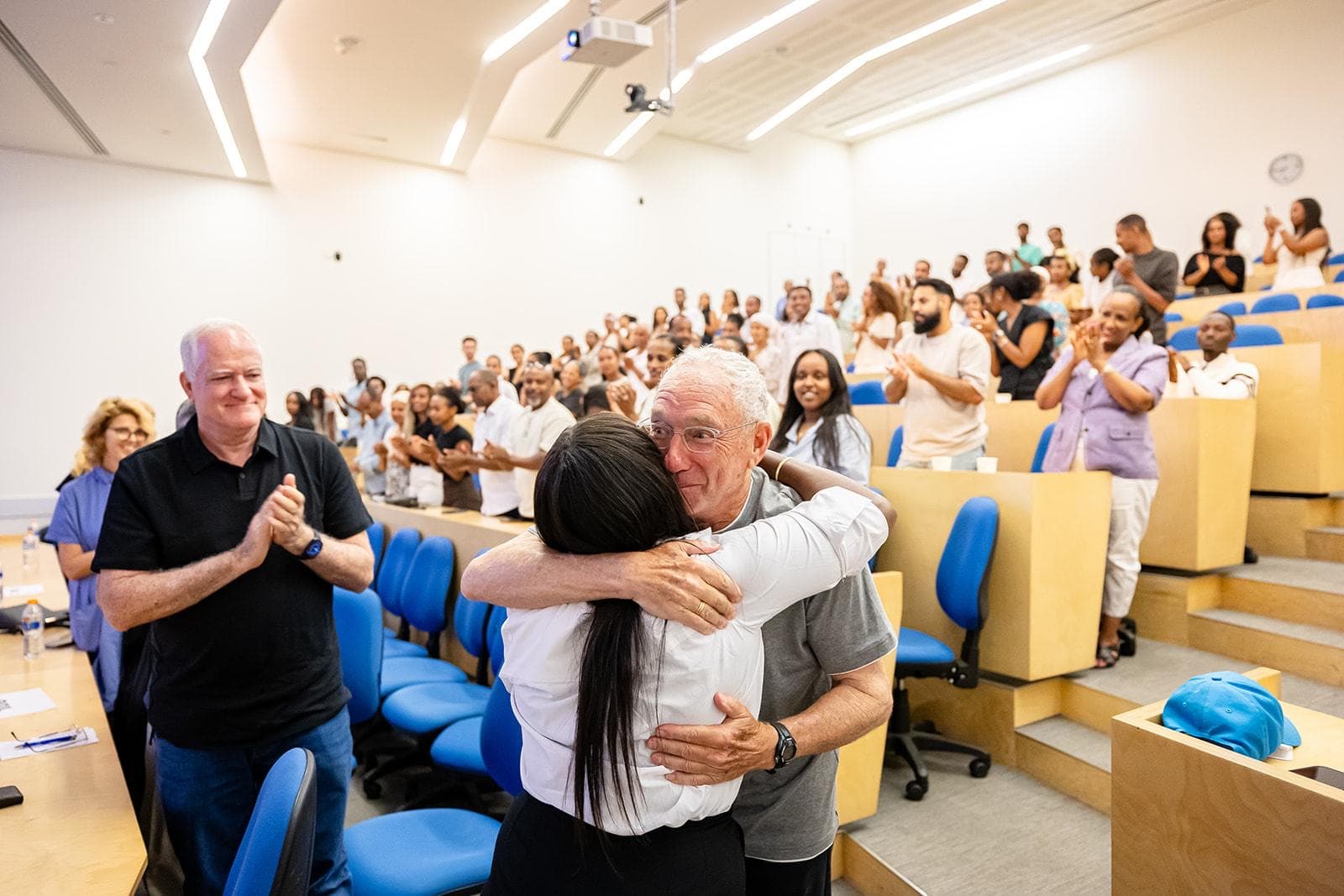 A graduate embraces Joey Low as the hall applauds.