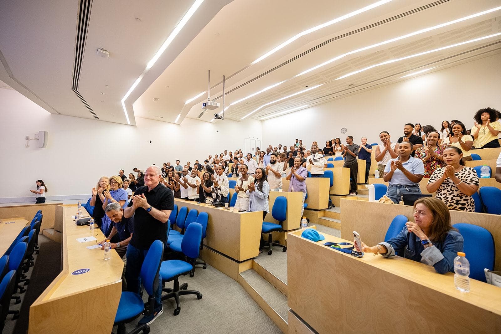 The full lecture hall on its feet, students and alumni applauding.