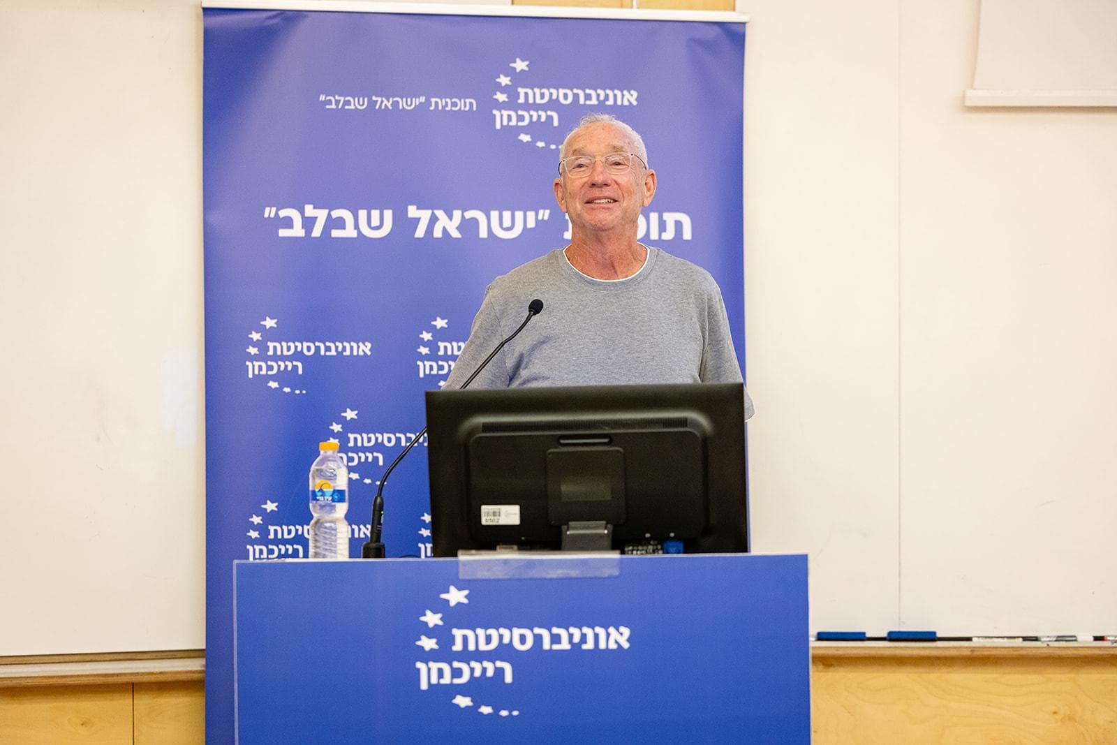 Joey Low speaking at a podium beside a Reichman University banner for the Israel at Heart program.