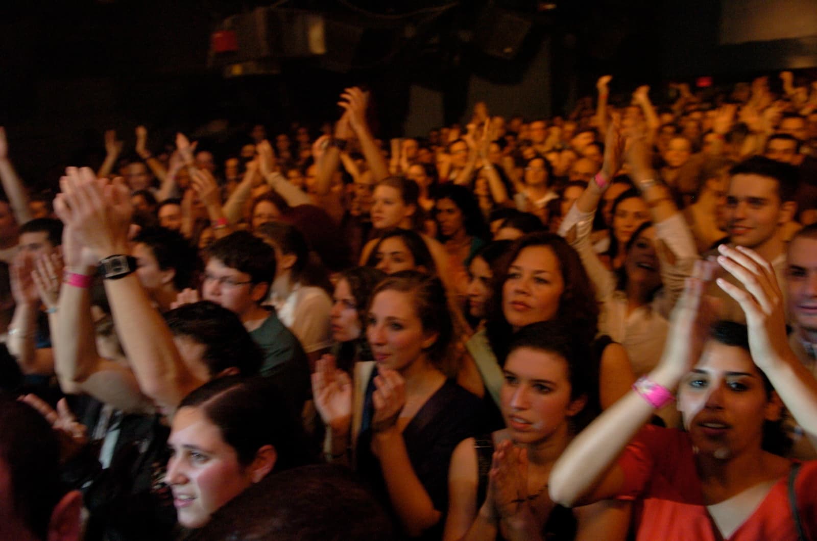 A sold-out crowd with hands raised, applauding during the concert.