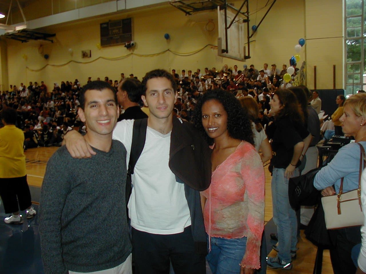 Three delegates, one of Ethiopian origin, standing together in a packed school gymnasium.