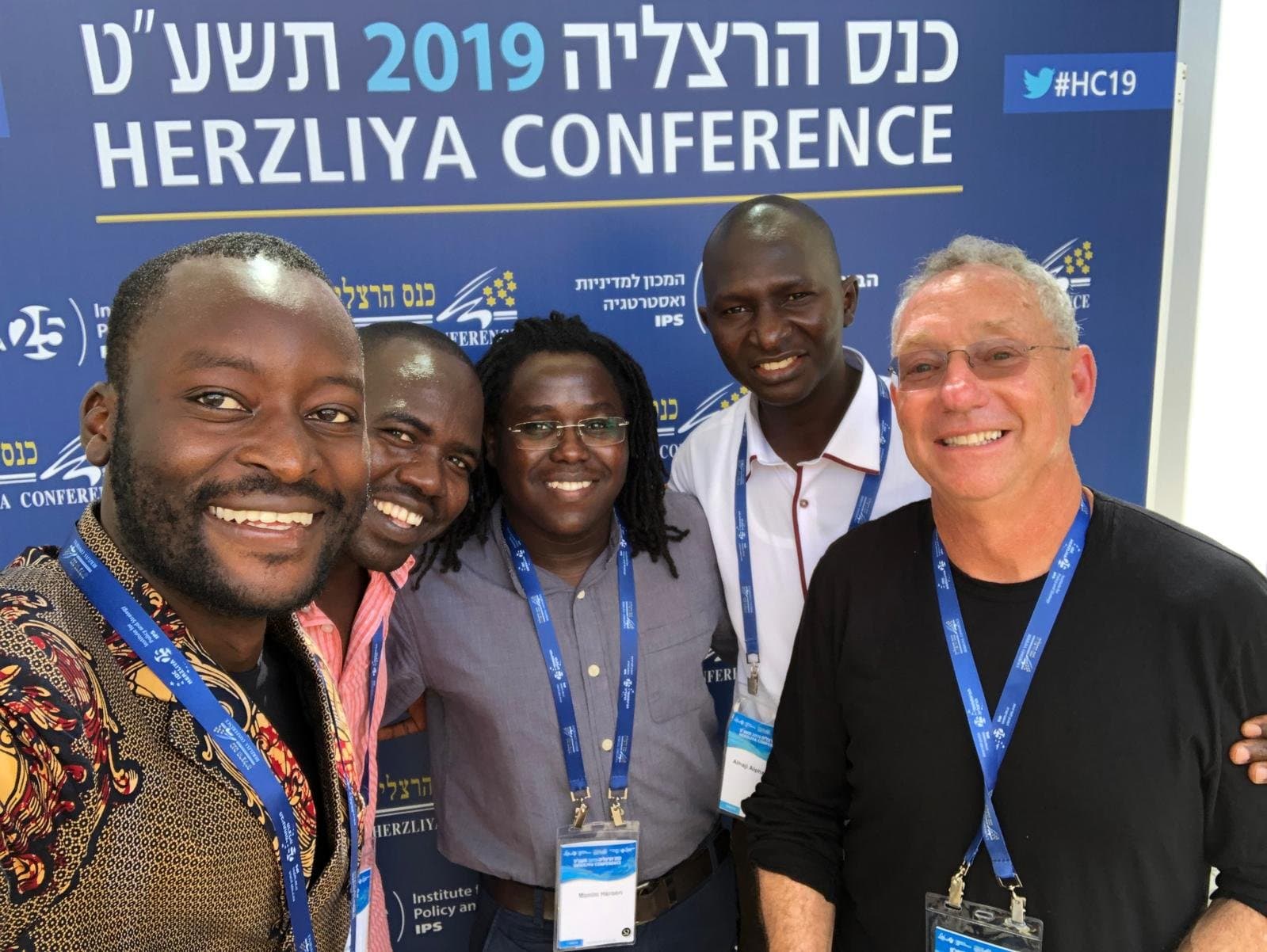 Members of the community at the Herzliya Conference, standing before the conference banner.