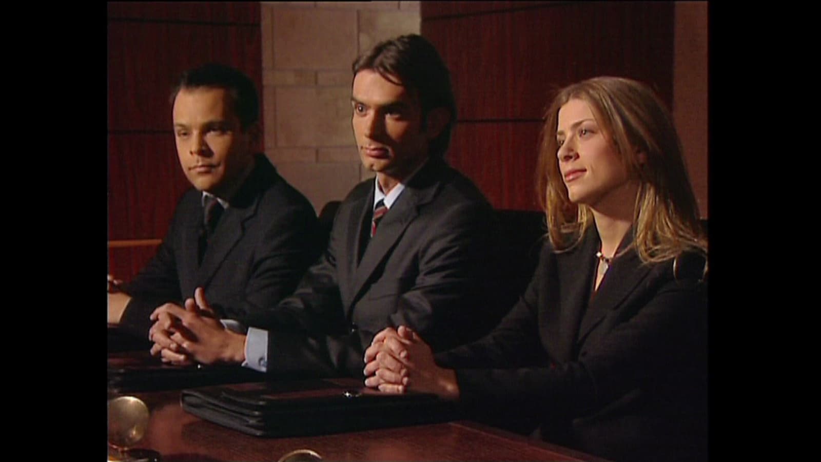 Three contestants seated closely together, composed under pressure.