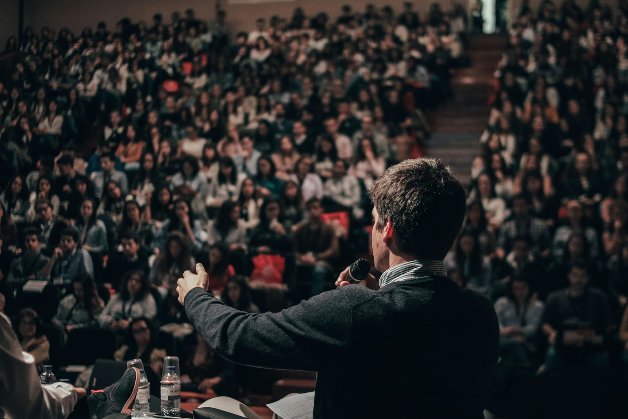 A speaker stands before a seated crowd, mid-sentence, the room leaning in to listen